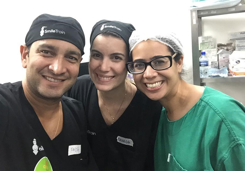 Camila sonríe con socios de Smile Train en uniformes médicos