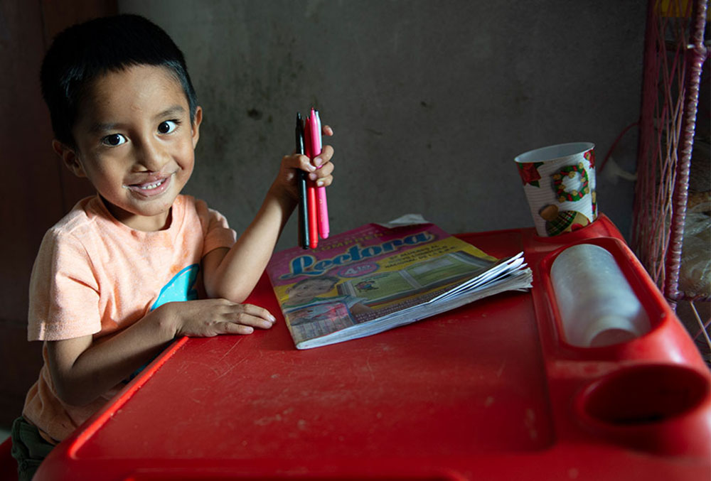 Aghelo smiling and drawing at his desk after cleft surgery