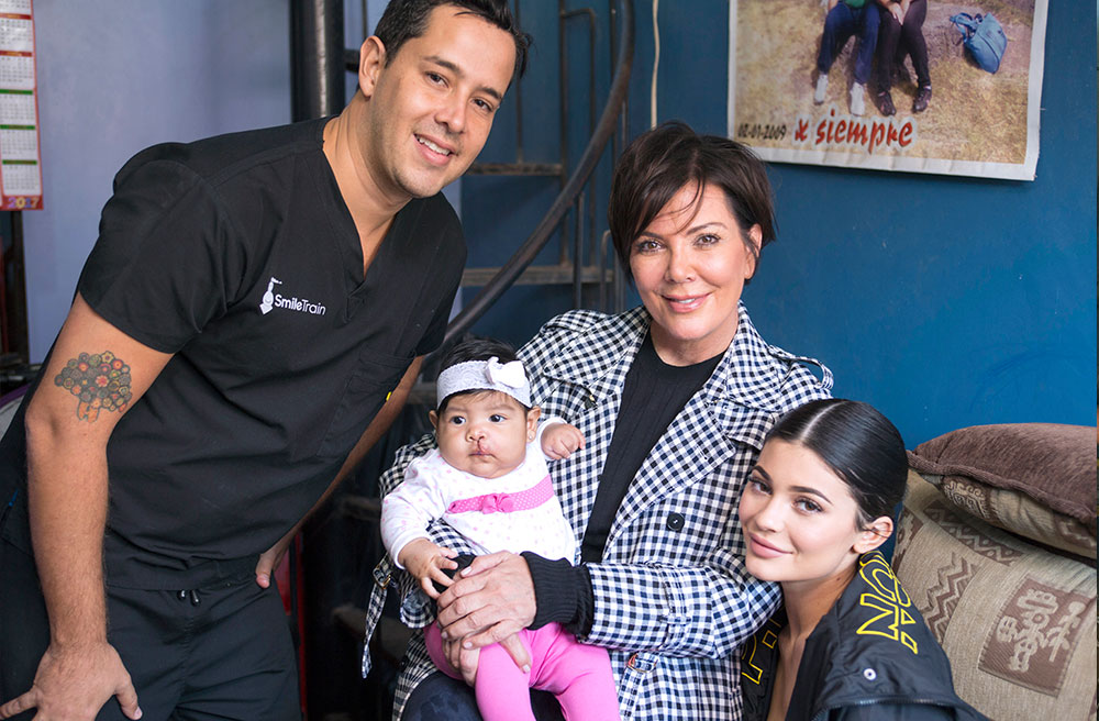 Kris Jenner smiling and holding Mia with Kylie and Smile Train's partner surgeon