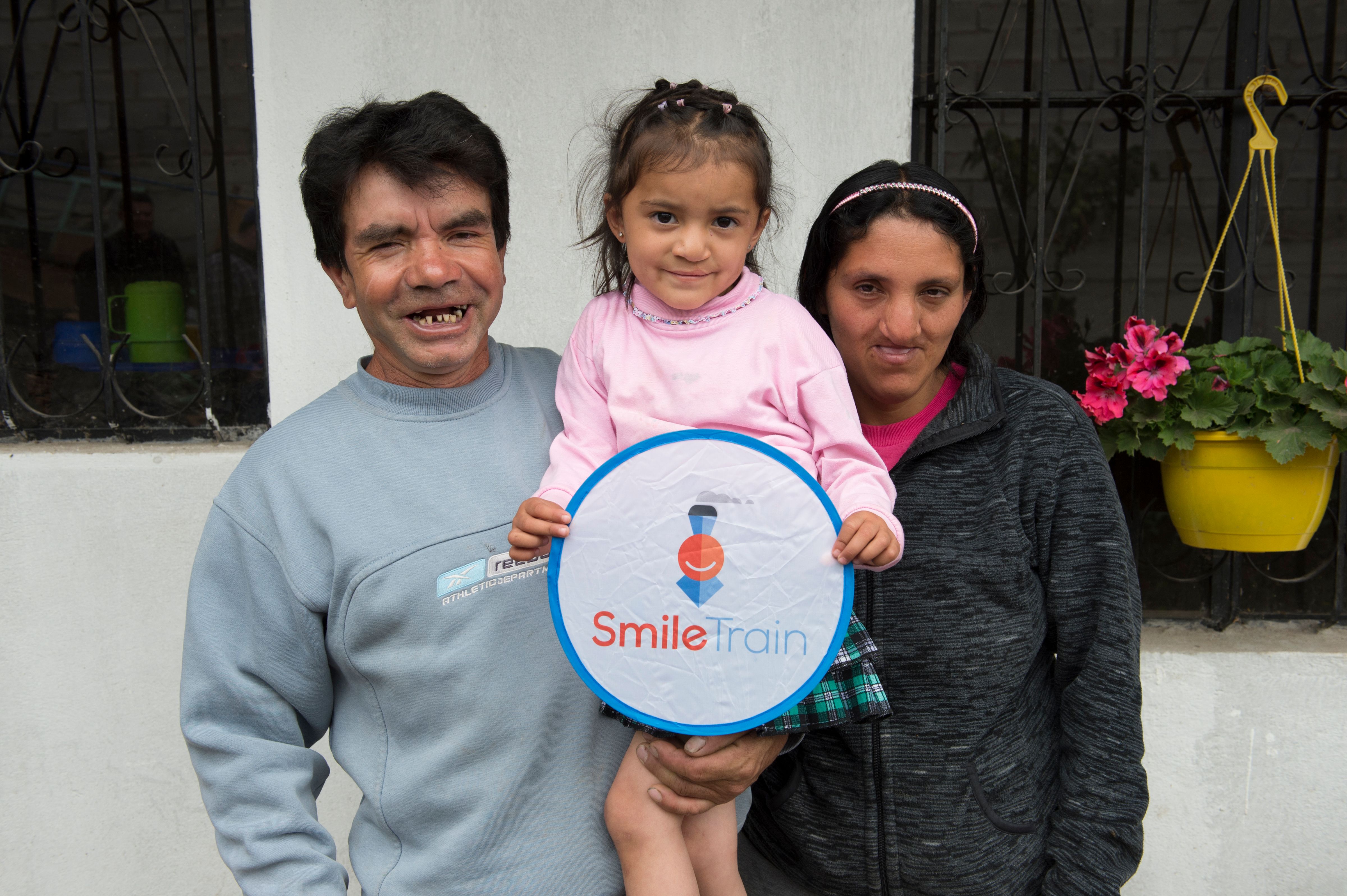 Estefanía y sus padres sonriendo y sosteniendo un cartel de Smile Train