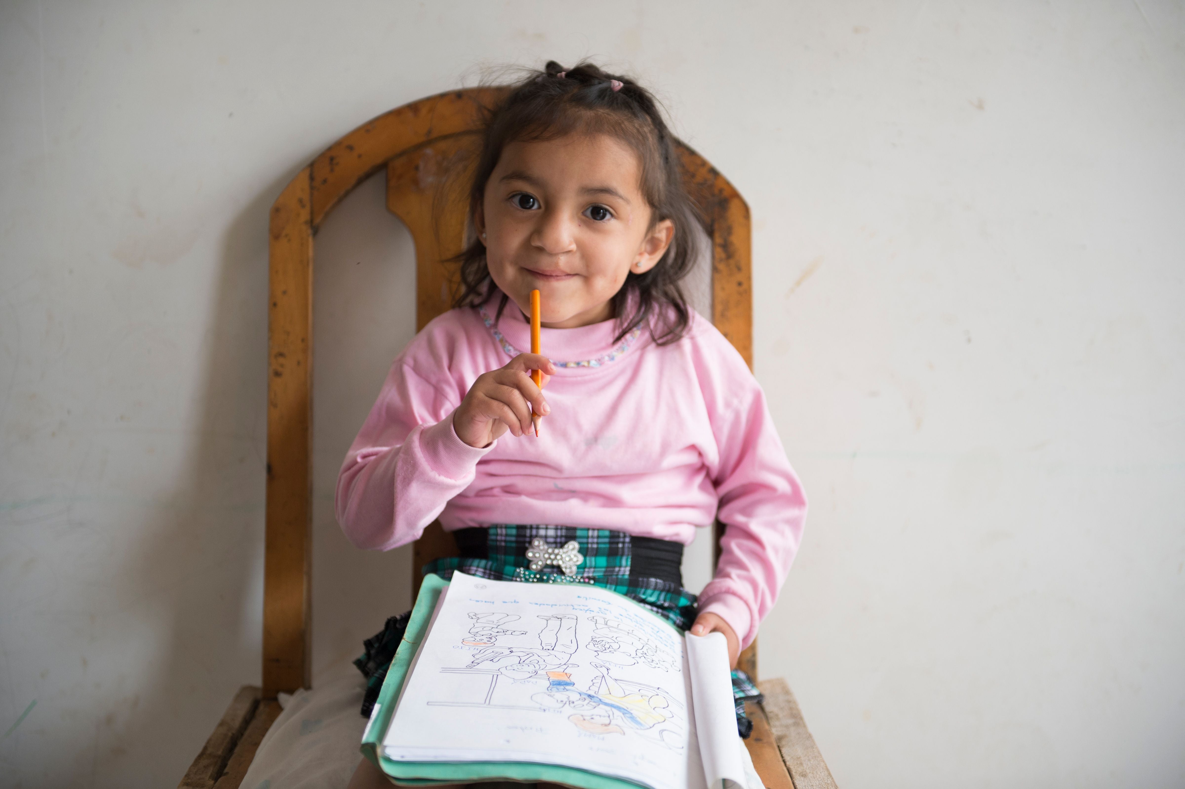 Estefania sonriendo y dibujando en su libro para colorear