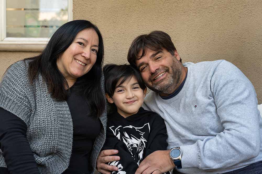 Tomas sits smiling between his mother and father, Denise and Yani