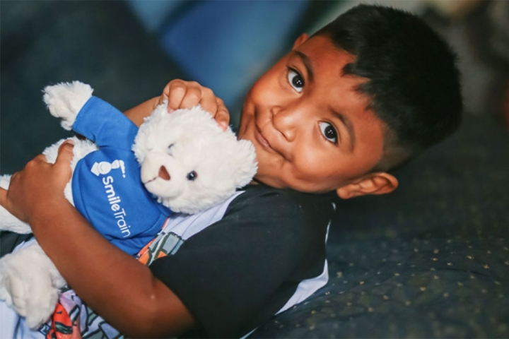 mathias smiling and holding his smile train teddy bear